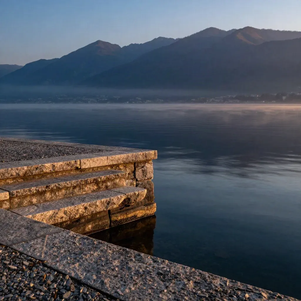 Riva del Lago di Como al crepuscolo con molo in granito e montagne sullo sfondo.